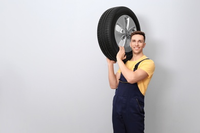 Photo of Male mechanic with car tire on light background