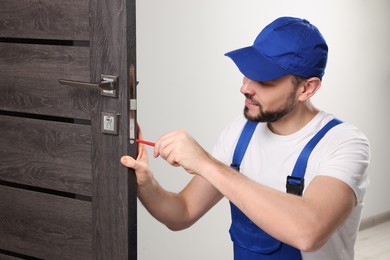Worker in uniform with screwdriver repairing door lock indoors