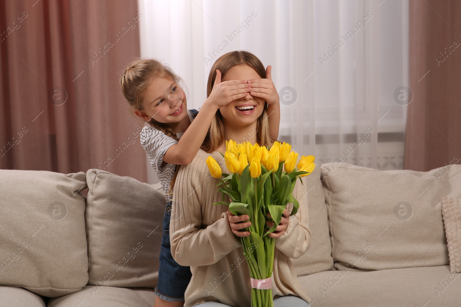 Photo of Little daughter congratulating mom with bouquet of yellow tulips at home. Happy Mother's Day