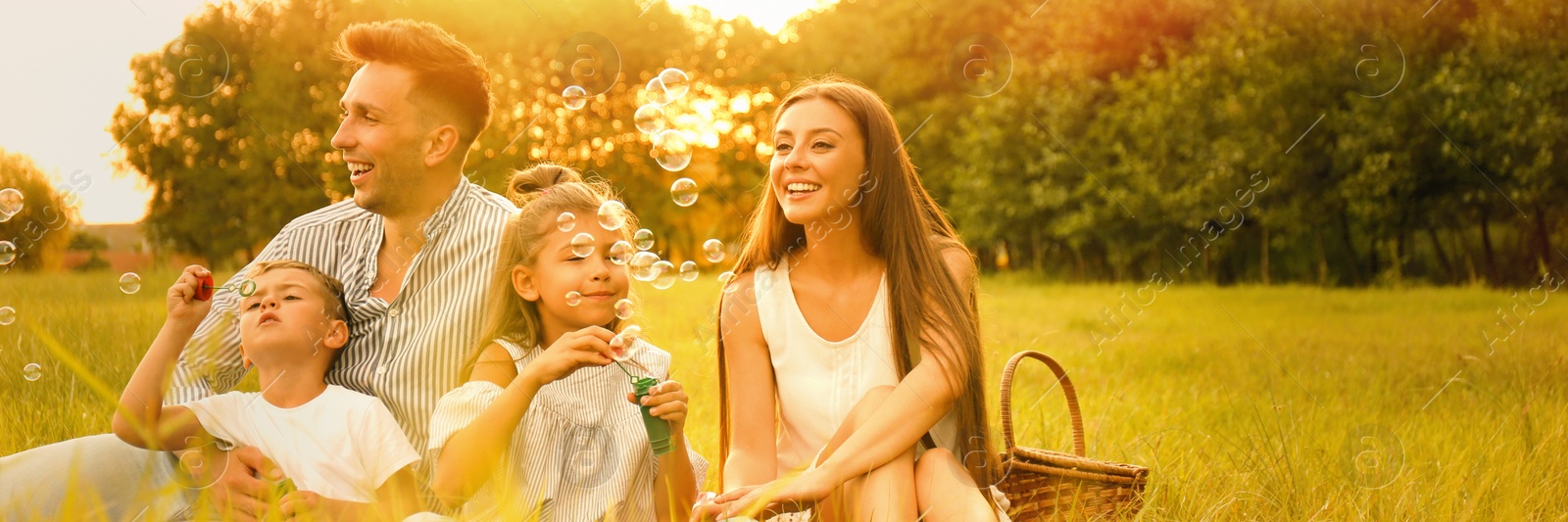 Image of Happy family blowing soap bubbles in park at sunset. Banner design