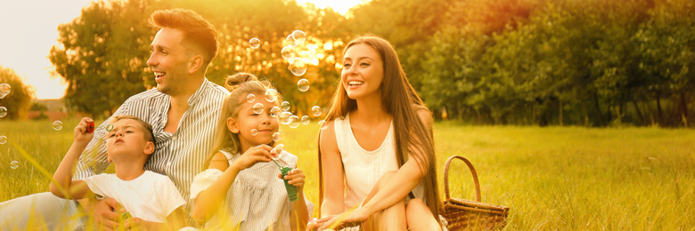Image of Happy family blowing soap bubbles in park at sunset. Banner design