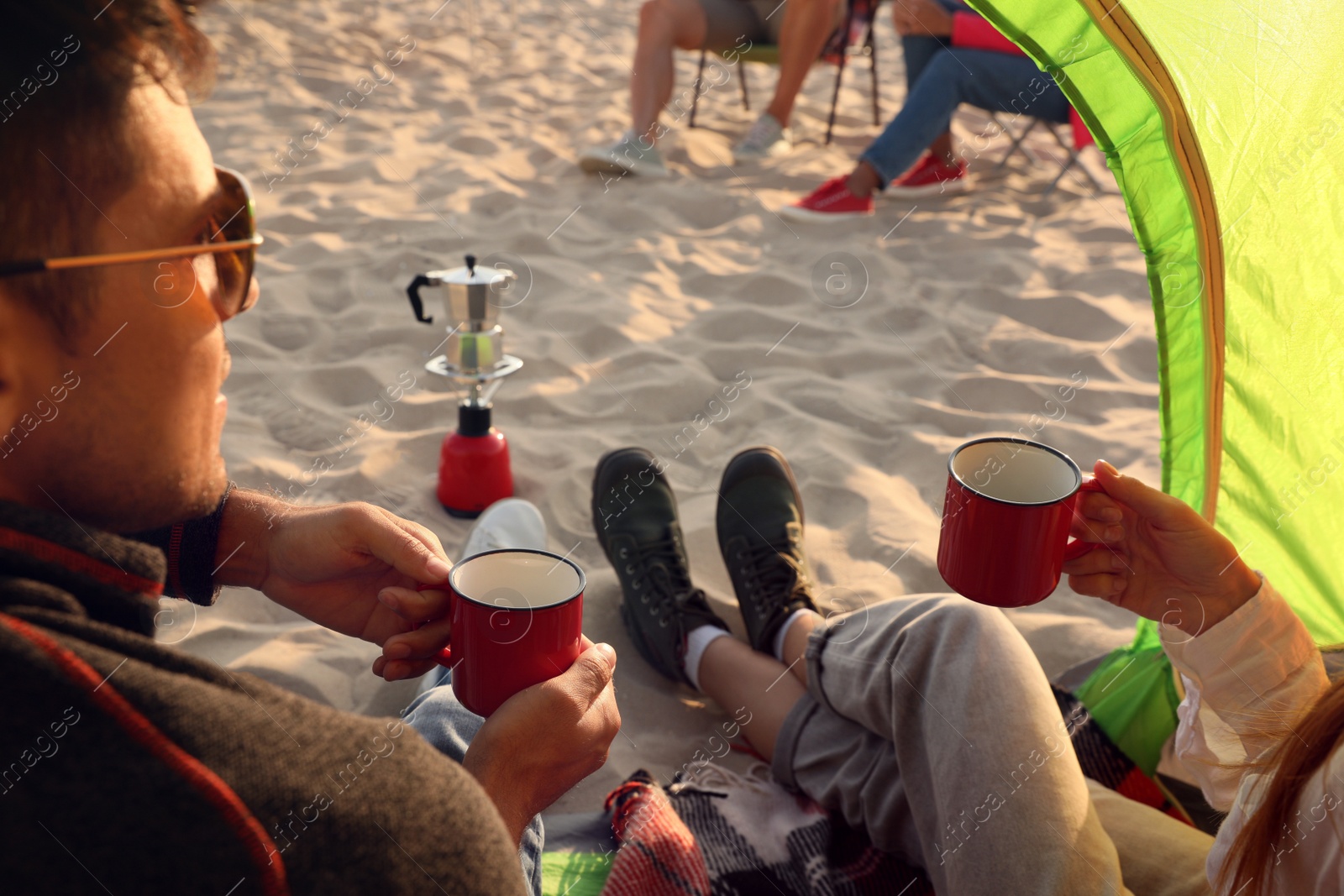 Photo of Friends resting on sandy beach, closeup. View from camping tent