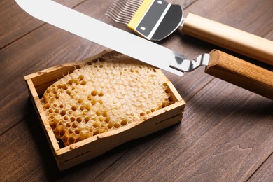 Photo of Honeycomb frame and beekeeping tools on wooden table, closeup