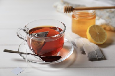 Photo of Tea bags, honey and lemon near cup of hot drink on white wooden table, closeup. Space for text
