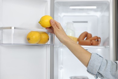 Photo of Young woman taking lemon out of refrigerator, closeup