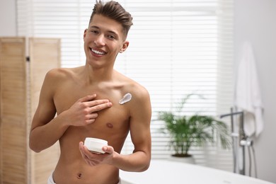 Handsome man applying moisturizing cream onto his shoulder in bathroom. Space for text