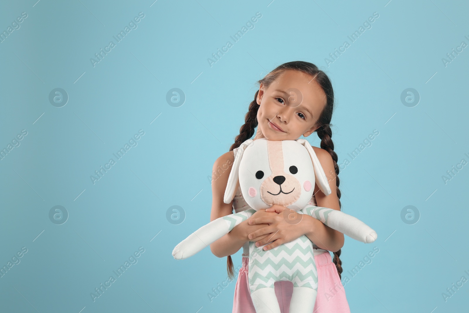 Photo of Cute girl wearing pajamas with toy on light blue background. Space for text