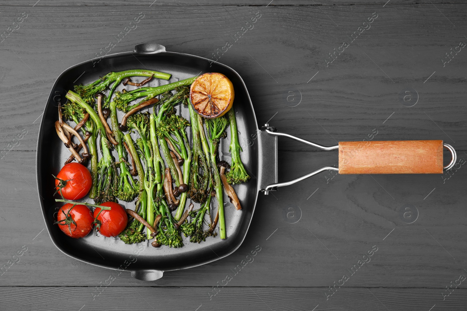 Photo of Grill pan with tasty cooked broccolini, mushrooms, tomatoes and lemon on grey wooden table, top view