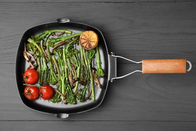 Grill pan with tasty cooked broccolini, mushrooms, tomatoes and lemon on grey wooden table, top view