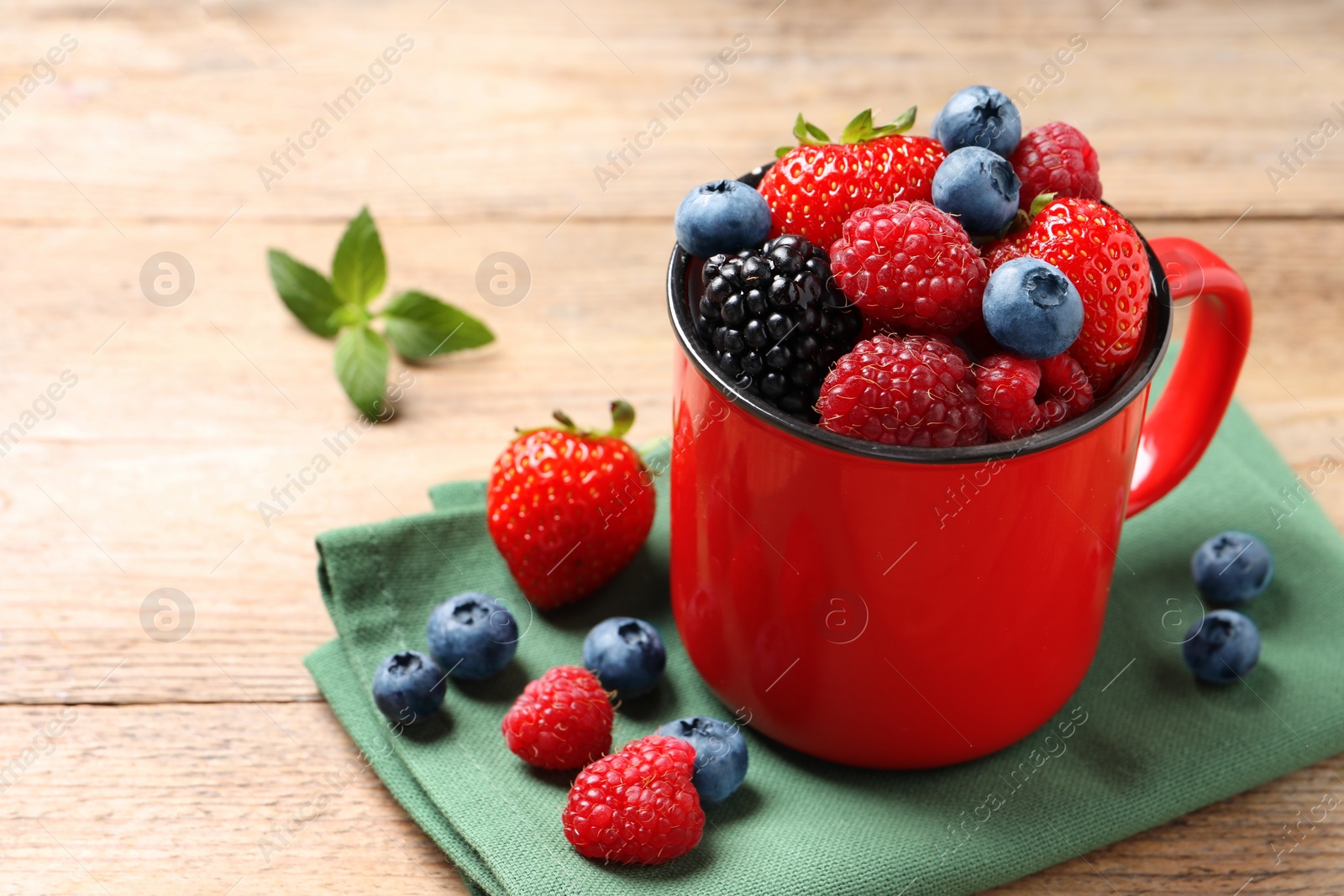 Photo of Many different fresh ripe berries in mug on wooden table, space for text