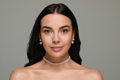 Photo of Young woman wearing elegant pearl jewelry on grey background