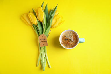 Photo of Aromatic coffee, beautiful flowers and GOOD MORNING wish on yellow background, flat lay