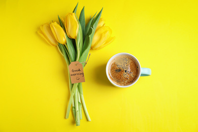 Aromatic coffee, beautiful flowers and GOOD MORNING wish on yellow background, flat lay