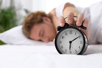 Photo of Sleepy man turning off alarm clock in morning, space for text. Bedtime