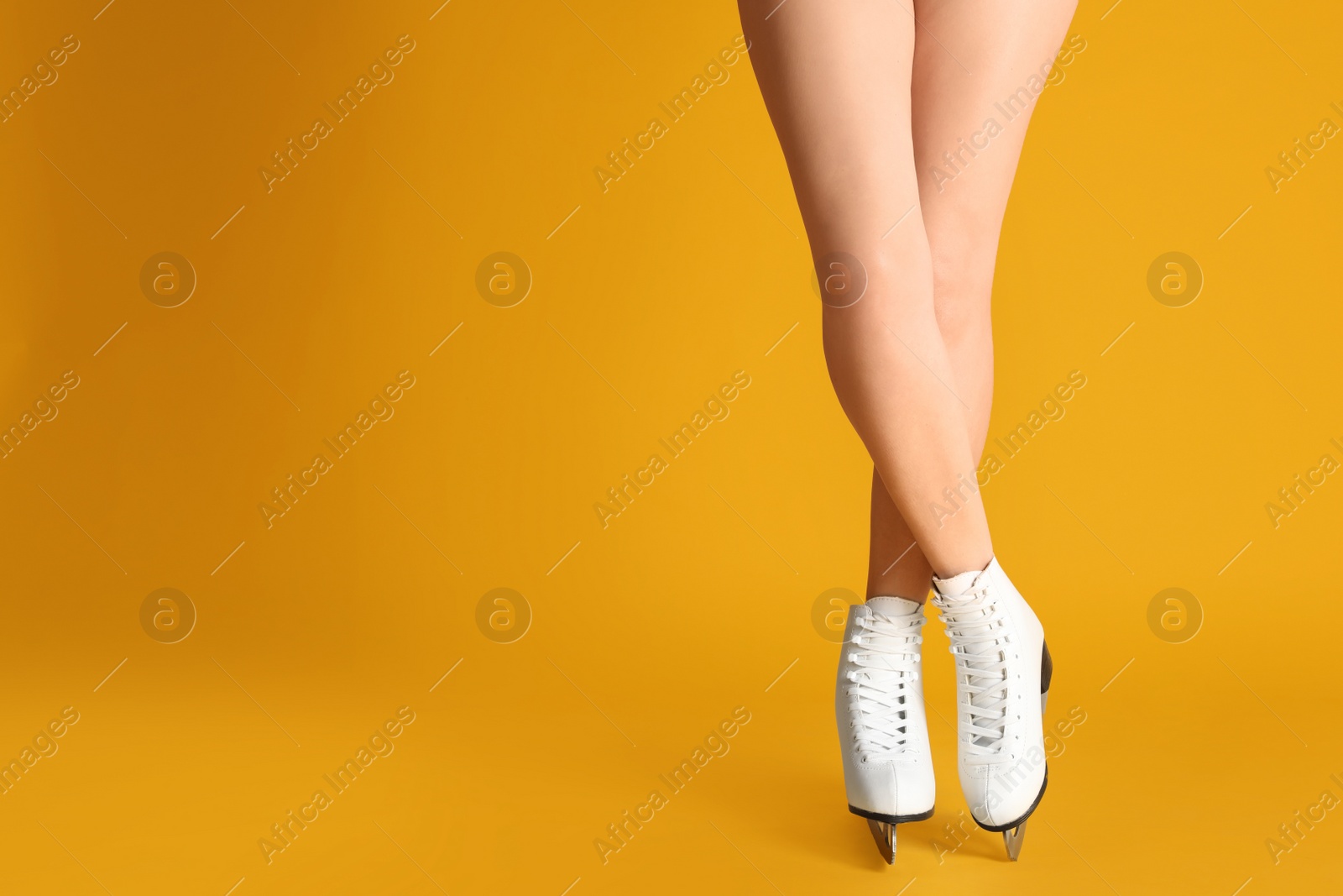 Photo of Woman in elegant white ice skates on yellow background, closeup of legs. Space for text