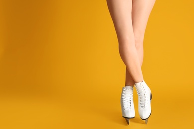 Woman in elegant white ice skates on yellow background, closeup of legs. Space for text