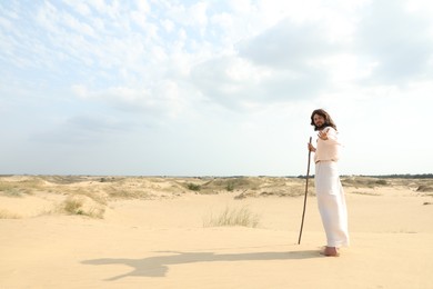 Photo of Jesus Christ walking with stick in desert. Space for text