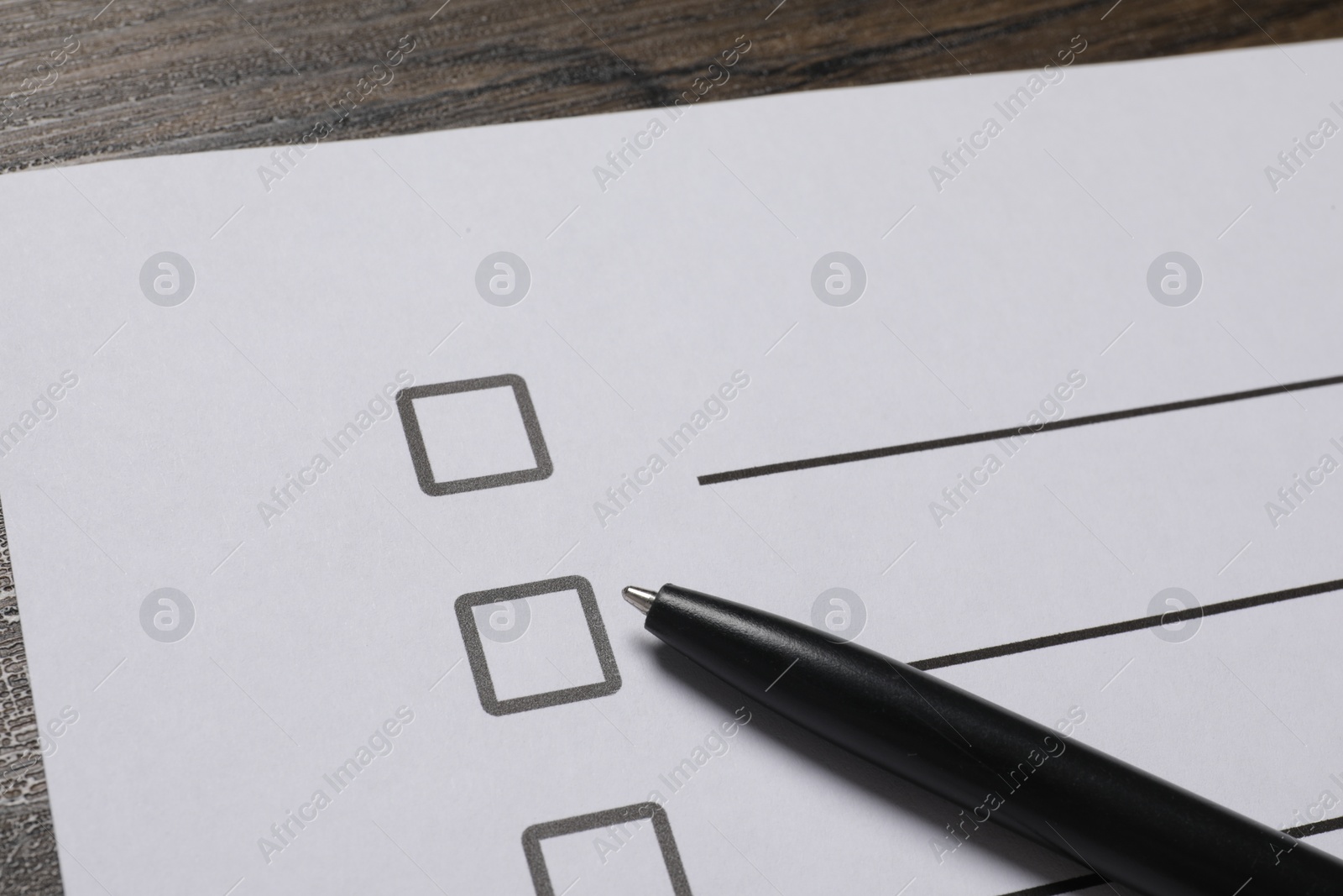 Photo of Paper sheet with checkboxes and pen on wooden table, closeup. Checklist