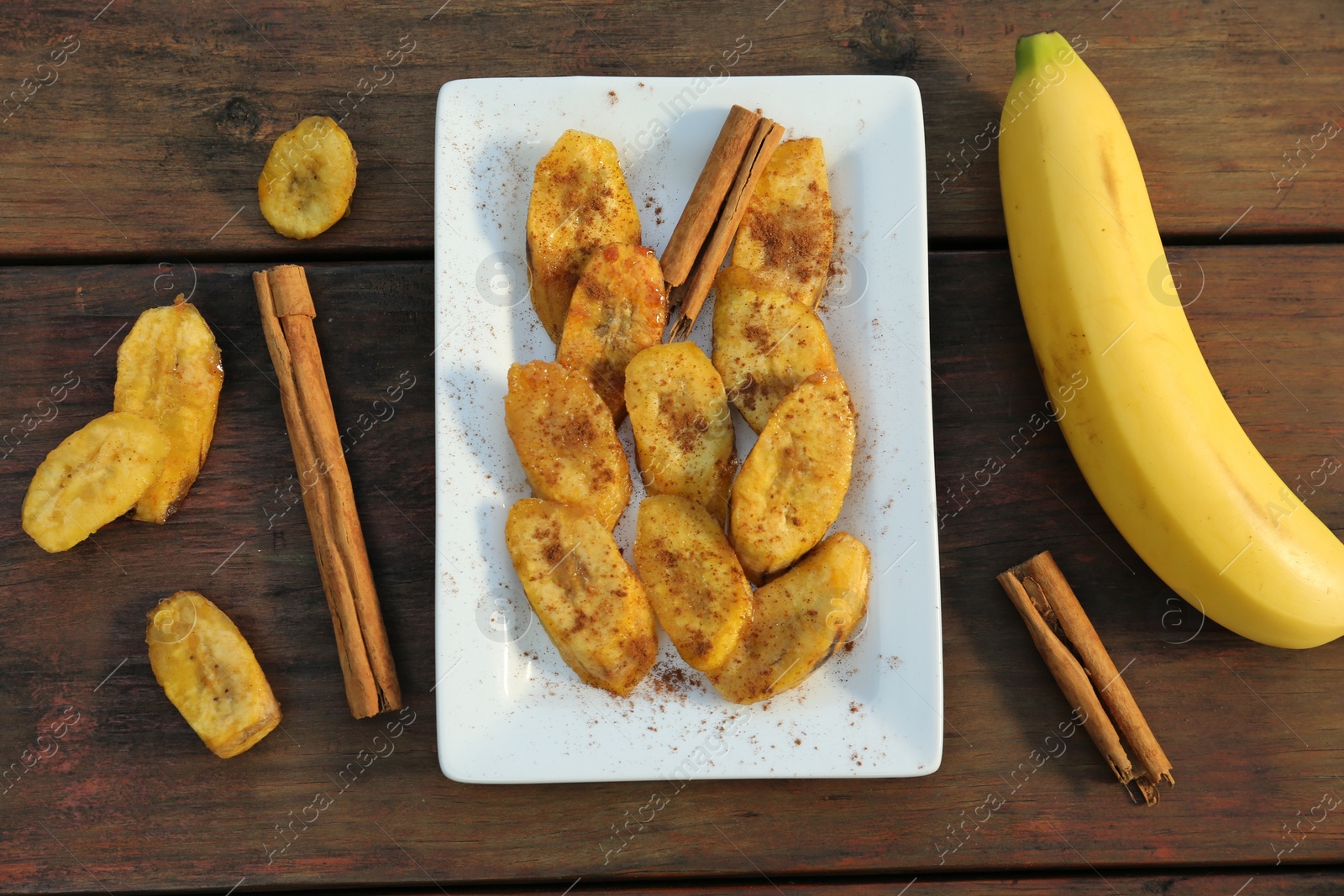 Photo of Tasty deep fried banana slices and cinnamon sticks on wooden table, flat lay