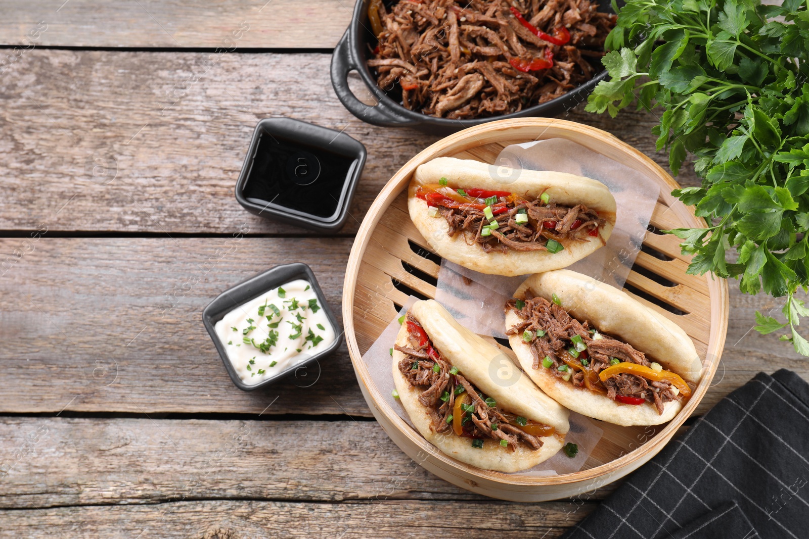 Photo of Delicious gua bao in bamboo steamer on wooden table, flat lay. Space for text