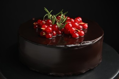 Photo of Tasty homemade chocolate cake with berries and rosemary on dessert stand against black background, closeup