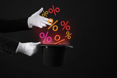 Image of Discount offer. Magician showing trick with percents signs flying out of top hat on black background, closeup