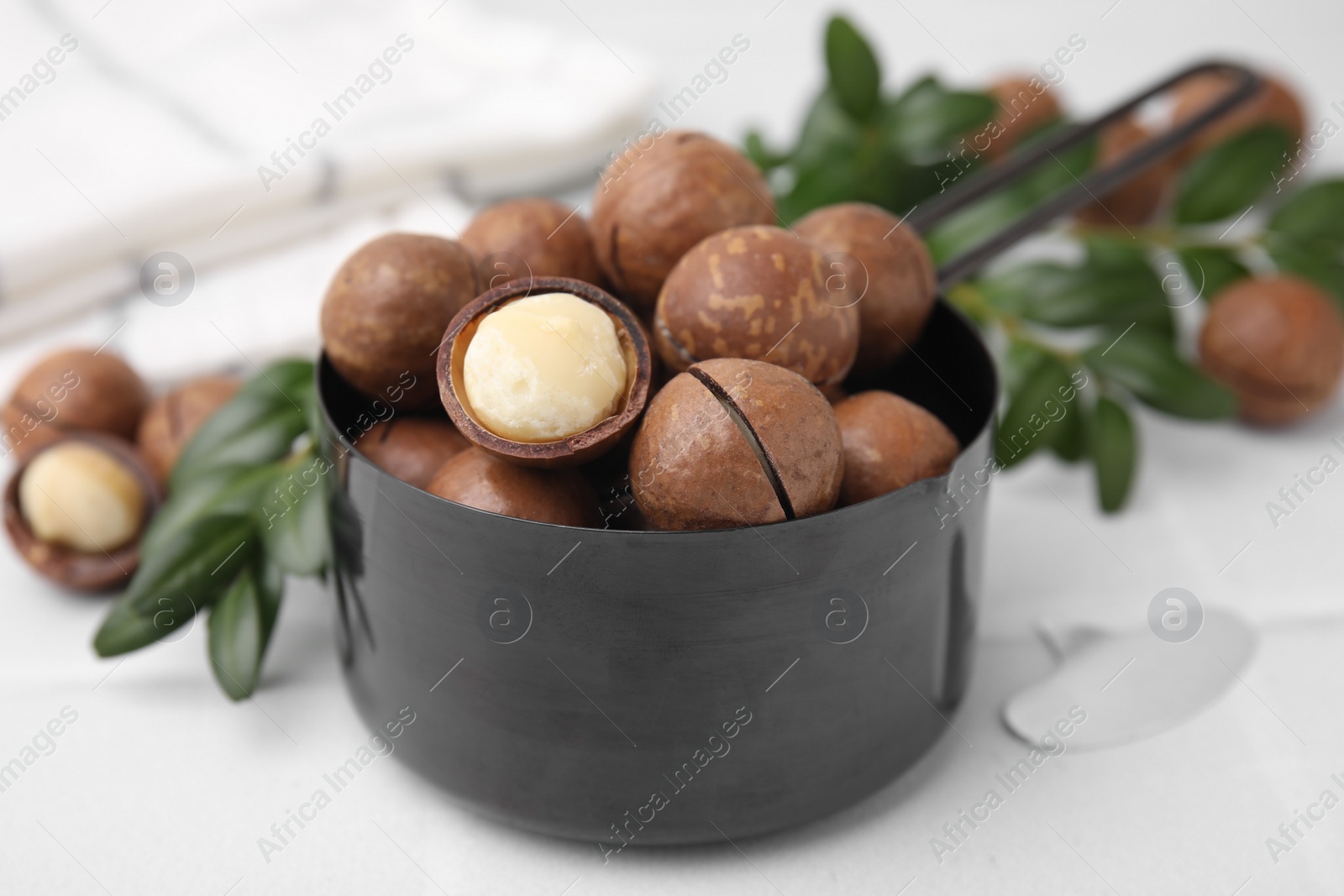 Photo of Tasty organic Macadamia nuts in small saucepan on white table, closeup