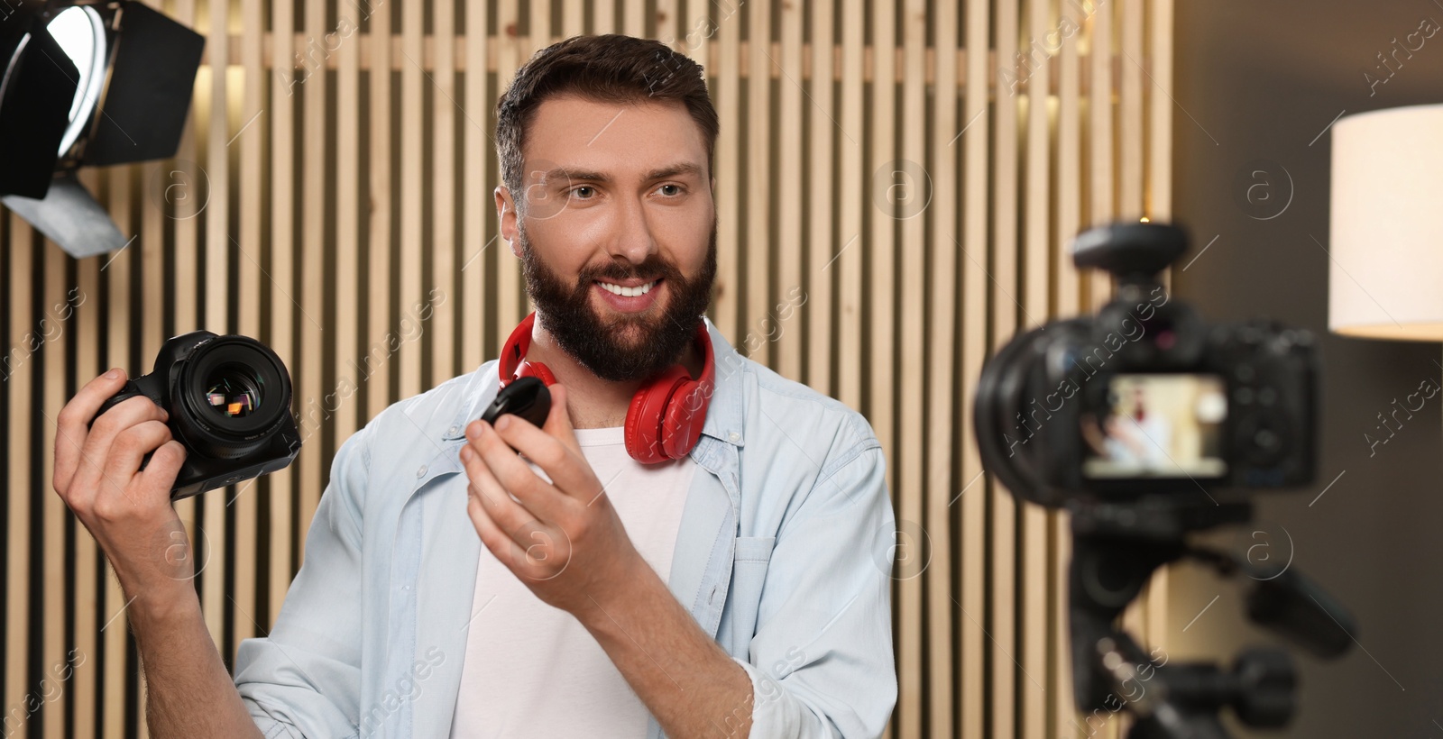 Photo of Smiling technology blogger with camera recording video review at home