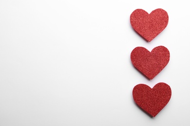 Red shiny paper hearts on white background, top view