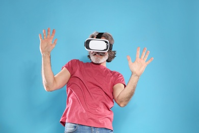 Emotional mature man playing video games with virtual reality headset on color background