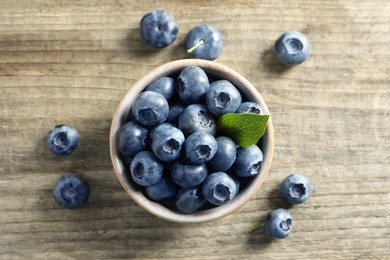 Photo of Bowl of fresh tasty blueberries on wooden table, flat lay