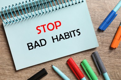 Image of Phrase Stop Bad Habits in notebook and pens on wooden table, flat lay