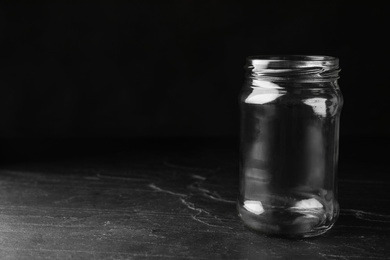 Photo of Empty glass jar on black stone table, space for text