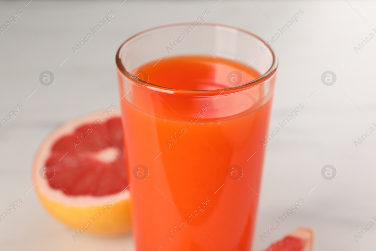 Photo of Tasty grapefruit juice in glass and fresh fruit on white table, closeup