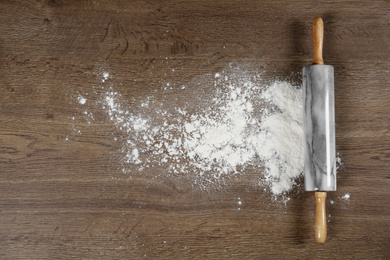 Photo of Flour and rolling pin on wooden table, flat lay