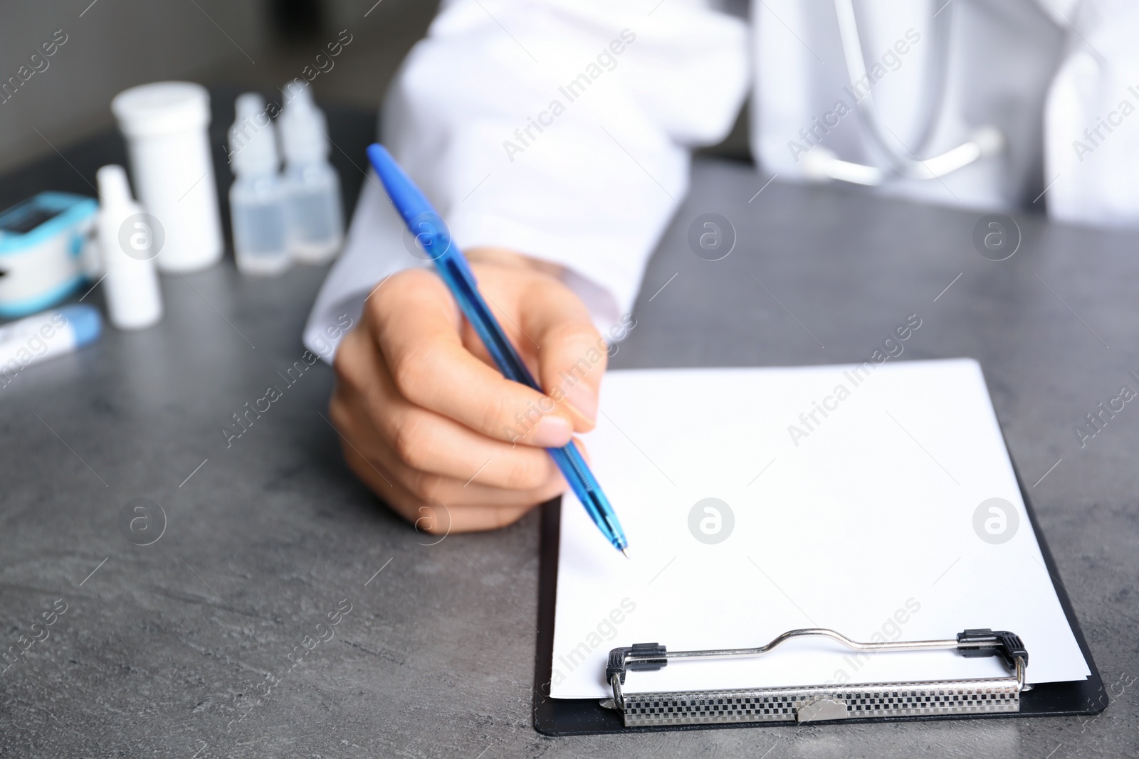 Photo of Doctor writing at table with different medical objects, closeup with space for text