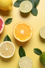 Photo of Different cut citrus fruits and leaves on yellow table, flat lay