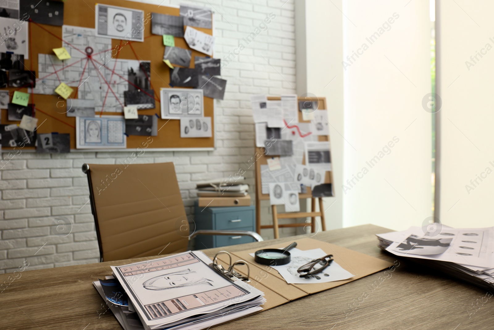 Photo of Papers with suspect's portrait, fingerprints and magnifying glass on wooden table in detective office