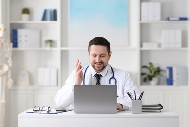 Photo of Doctor having online consultation via laptop at table in clinic