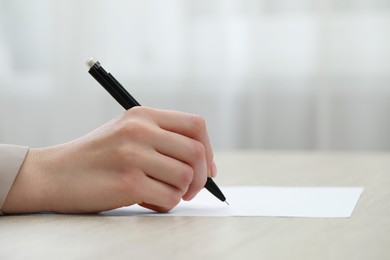 Photo of Woman writing on sheet of paper at wooden table, closeup