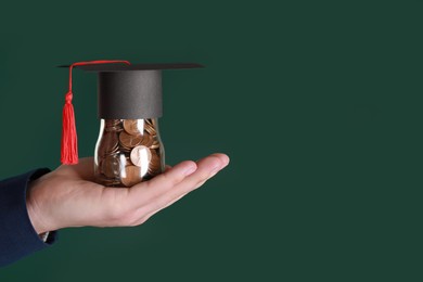 Photo of Man holding glass jar of coins and graduation cap against green background, closeup with space for text. Scholarship concept