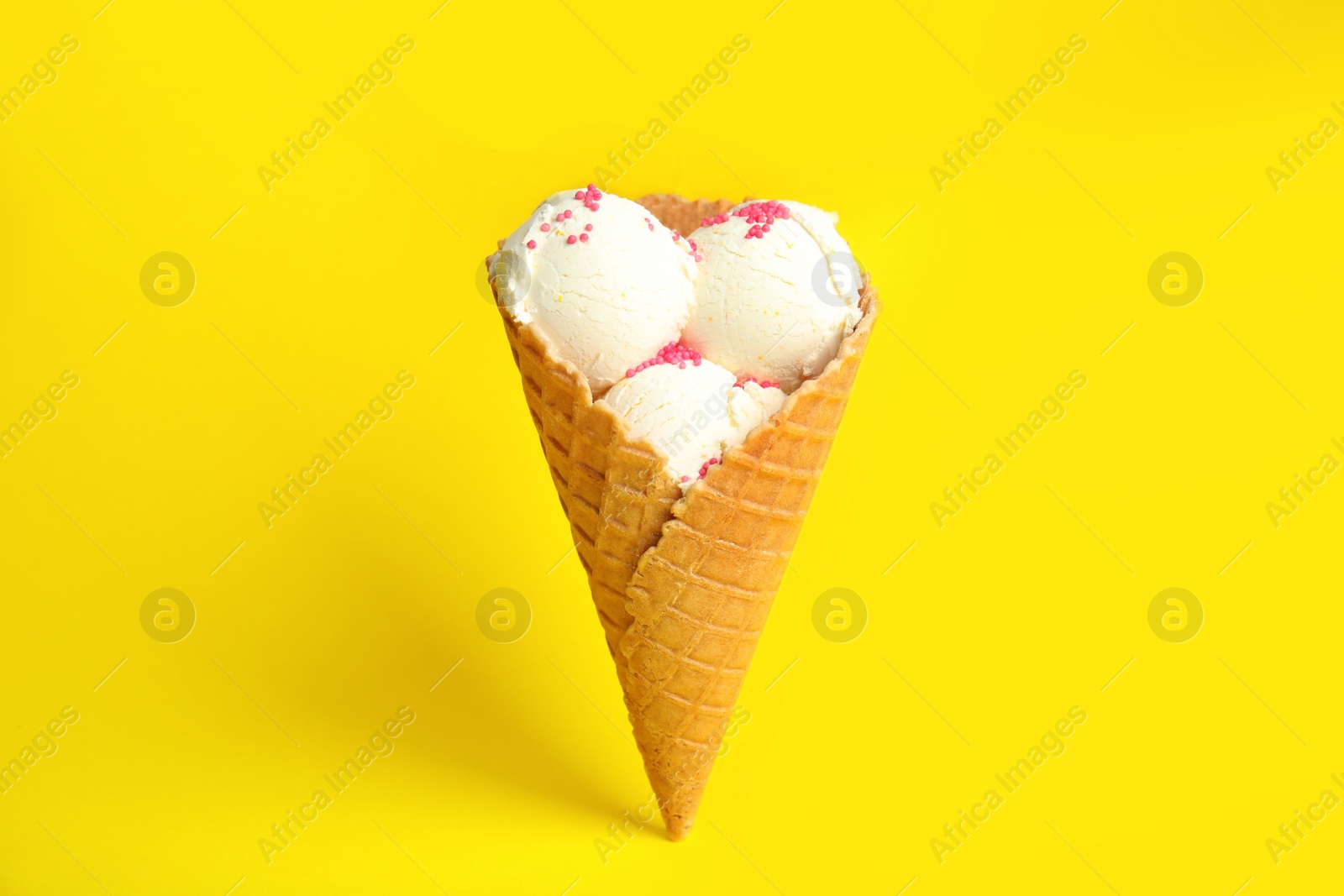 Photo of Delicious vanilla ice cream in wafer cone on yellow background