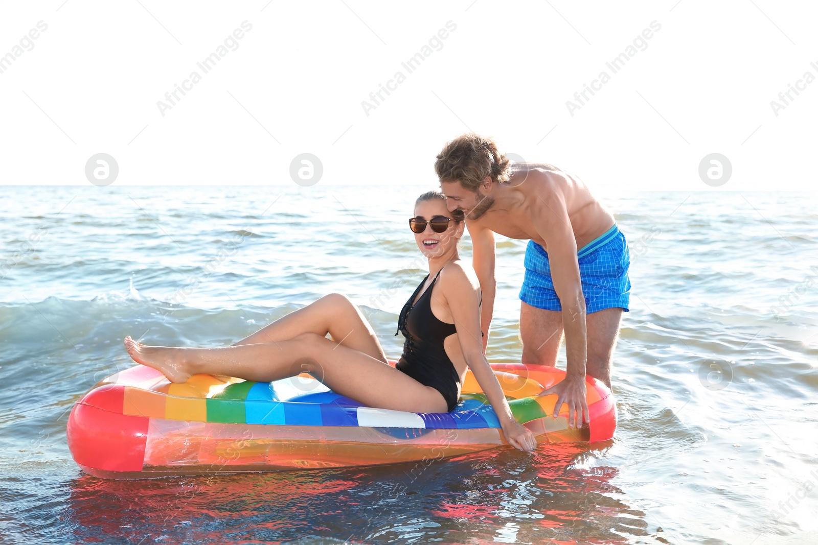 Photo of Happy young couple in beachwear swimming with inflatable mattress in sea