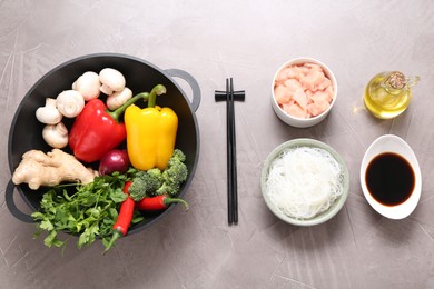 Photo of Wok, chopsticks and different products on grey textured table, flat lay