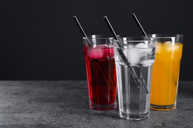 Glasses of different refreshing soda water with ice cubes and straws on grey table, space for text