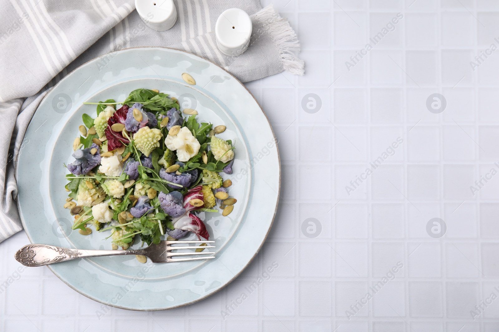 Photo of Delicious salad with cauliflower and pumpkin seeds served on white tiled table, flat lay. Space for text