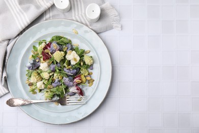 Photo of Delicious salad with cauliflower and pumpkin seeds served on white tiled table, flat lay. Space for text