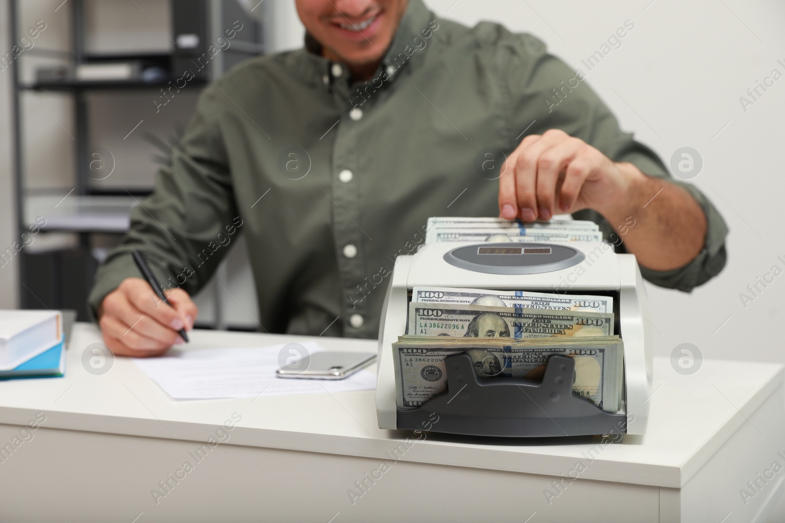 Photo of Man using banknote counter at white table indoors, closeup
