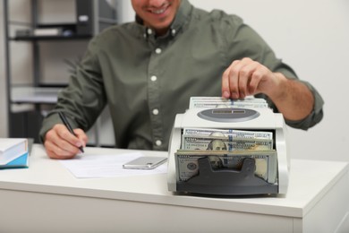 Man using banknote counter at white table indoors, closeup