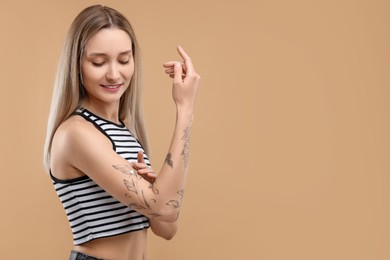 Tattooed woman applying cream onto her arm on beige background, space for text
